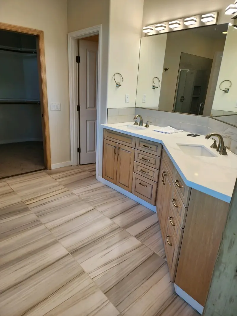 Bathroom with a corner double vanity in wood cabinets and a wood-look tile floor