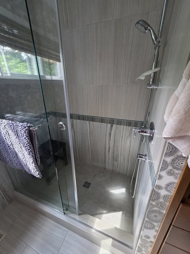 Glass-enclosed shower with large grey wall tile, a mosaic accent strip and a corner bench