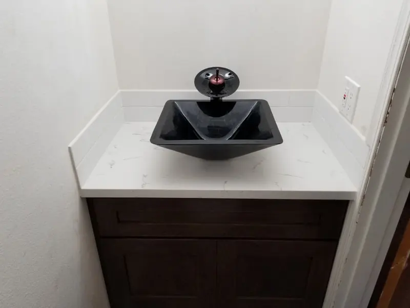 Dark wood vanity with a white stone-look top and a black glass vessel sink