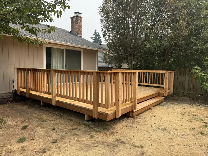 New wood deck with picket railing and wide steps across the back of a single-storey house