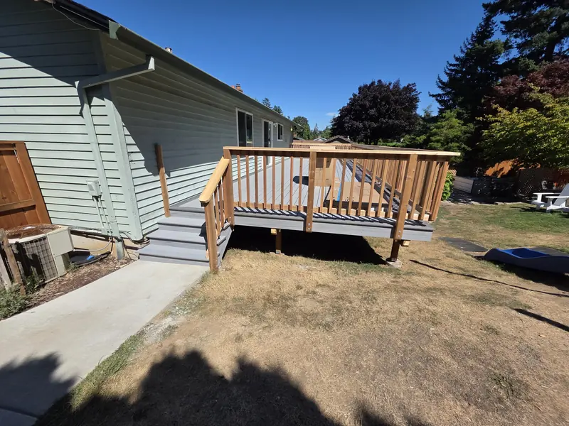 Low wood deck with railing and steps off the side of a pale green house