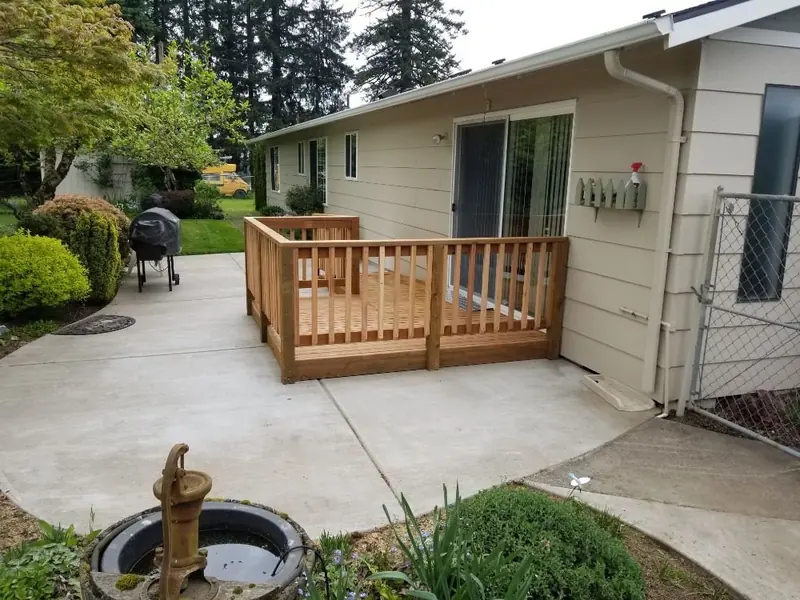 Small wood deck with picket railing built off a concrete patio behind a beige house