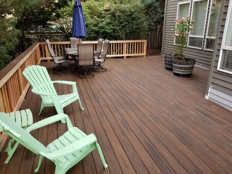 Stained wood deck with railing, a patio table and green Adirondack chairs