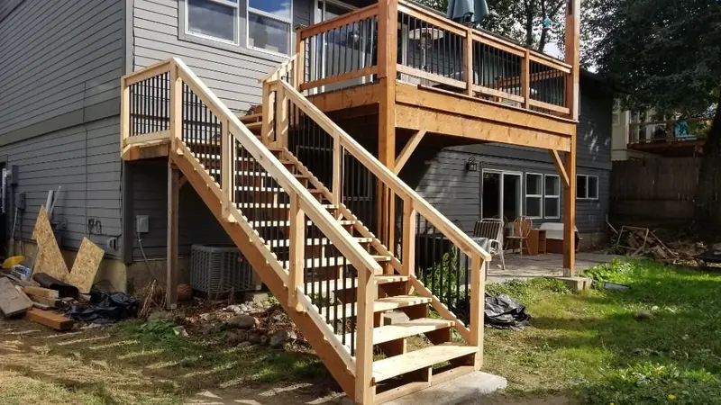 Two-level wood deck with a long exterior stair and black balusters against grey siding