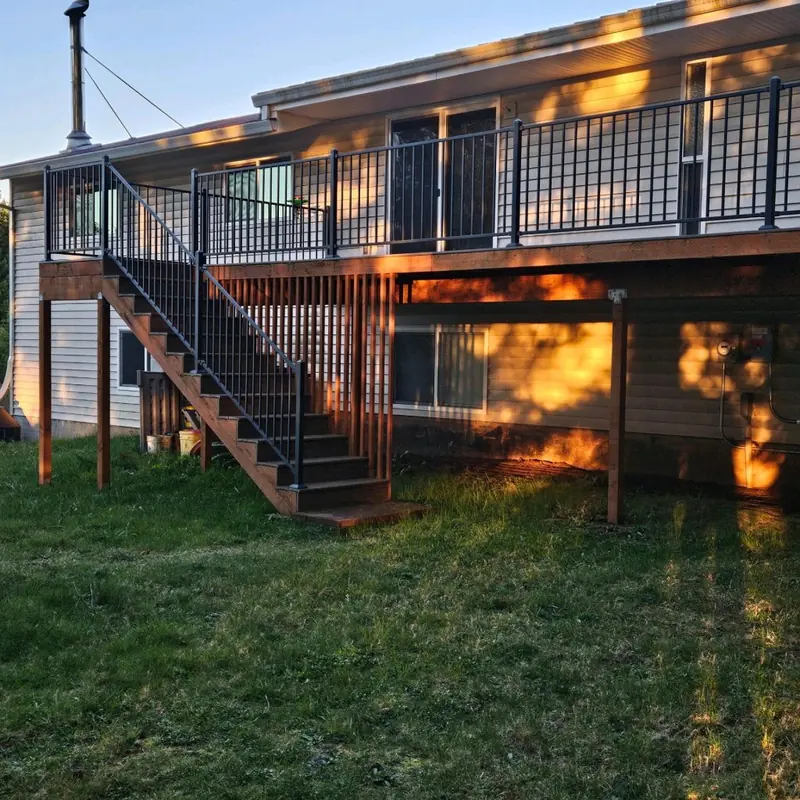 Second-storey wood deck with black metal balusters and a stair down to the lawn, in low evening sun