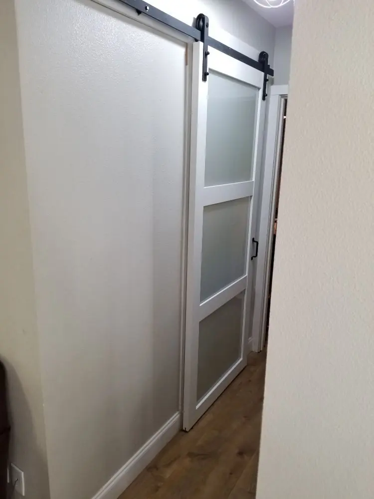 White sliding barn door with frosted panels on a black rail beside a wood-look floor
