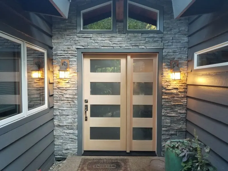 Double front doors with frosted glass panels, set in a stacked-stone wall between two lit lanterns