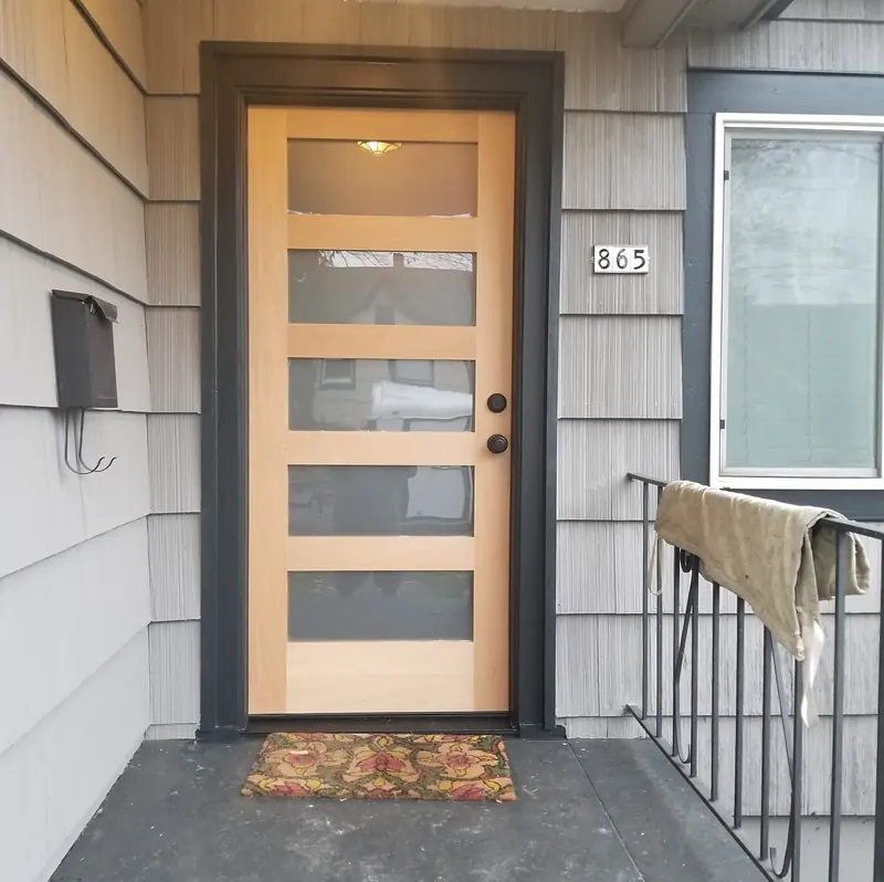 Wood front door with five frosted glass panels in a black frame, beside grey shingle siding
