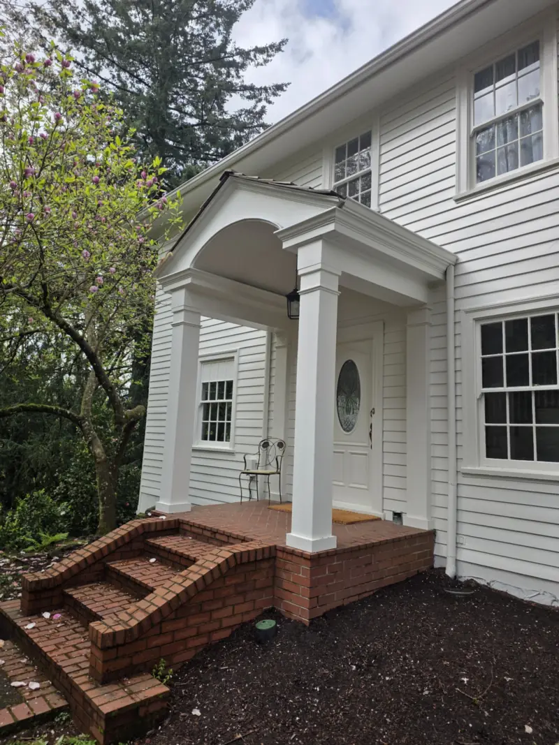 Arched entry portico with white columns over curved brick steps on a white two-storey house