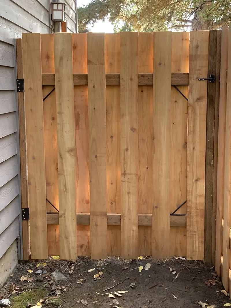 Cedar gate with black hinges and a latch, next to grey siding