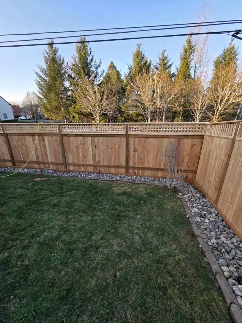 Wood privacy fence with a lattice top around a lawn edged in river rock