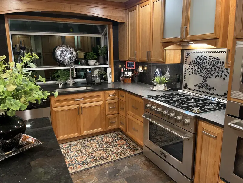 Wood cabinets around a stainless gas range, with a garden window over the sink and a tree-design tile backsplash