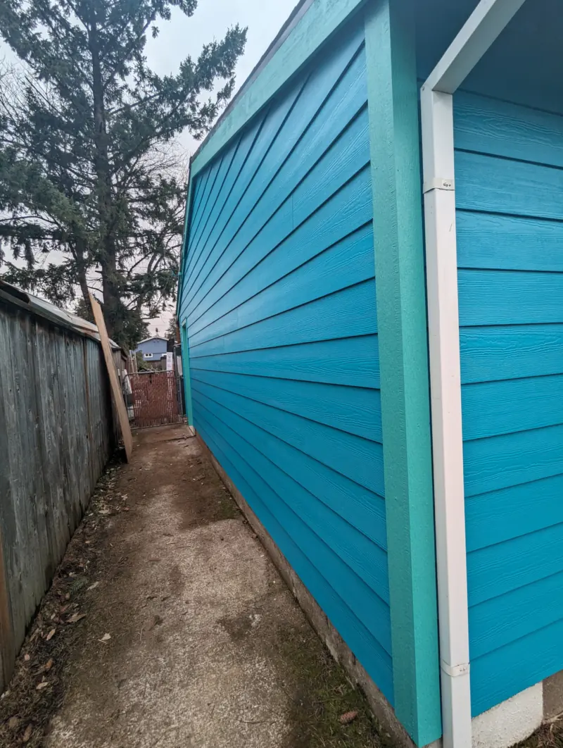Narrow side of the house in fresh turquoise paint with white corner trim, beside a wood fence