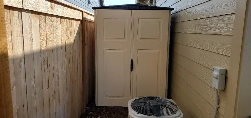 Small storage shed with double doors tucked between a wood fence and the house