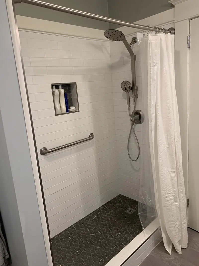 Walk-in shower with a horizontal grab bar, a tiled niche and a handheld shower head