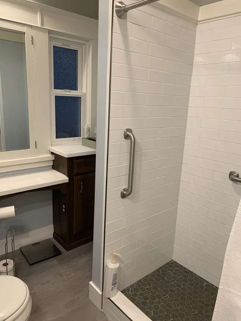 Bathroom with a walk-in shower, vertical grab bar and new wood-look floor beside the vanity
