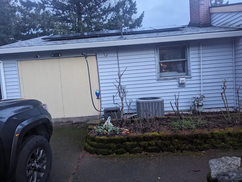 Before: back wall of the house in old white vinyl siding, with an air-conditioning unit and garden bed