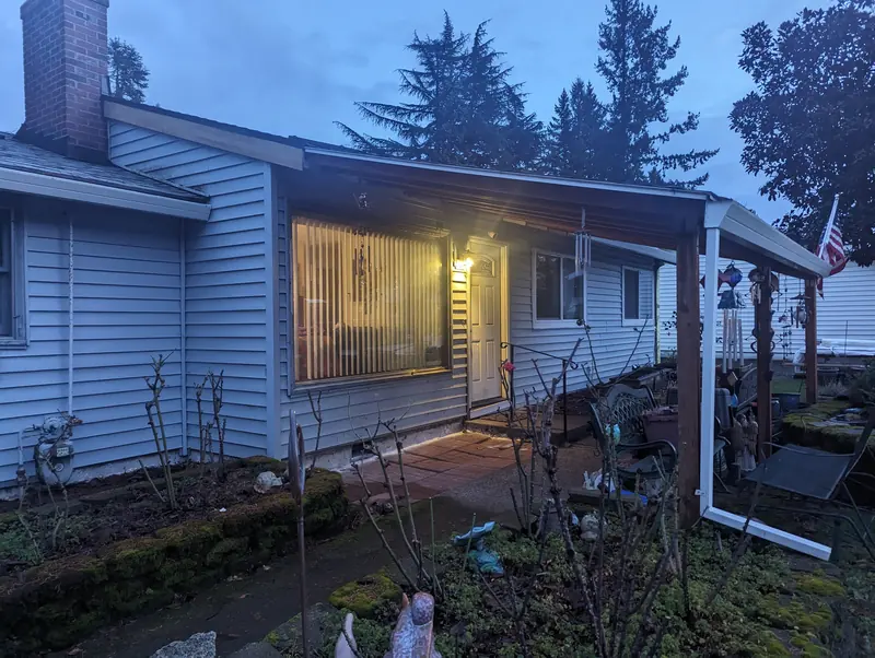 Before: the front of the house with its old pale vinyl siding and covered porch, at dusk