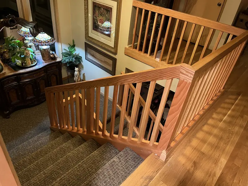 Wood railing with square balusters turning down a carpeted staircase