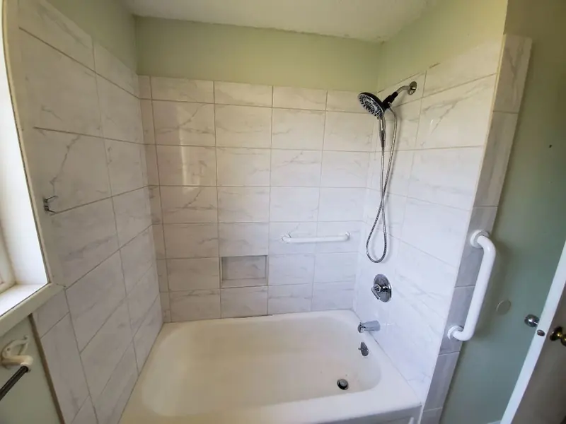 Bathtub surround in large marble-look tile with a vertical grab bar at the entry