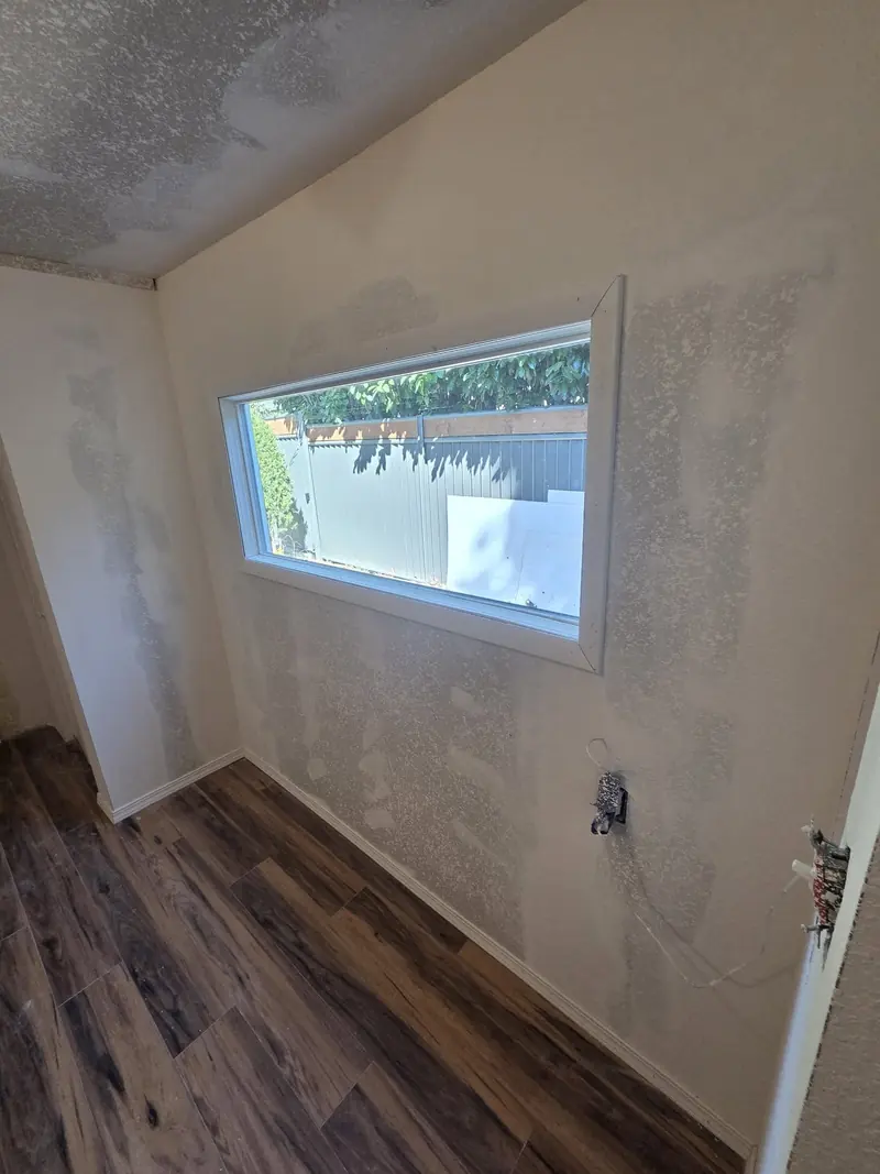 Wide window in a freshly mudded drywall wall above new wood-look plank flooring